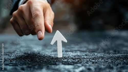 Closeup of a hand pointing at a white arrow on a textured surface, symbolizing growth or progress photo