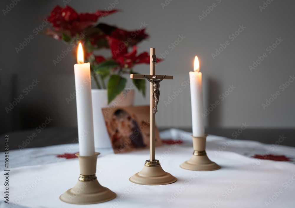cross with Jesus crucified and two lit candles on a white tablecloth with a Christmas tree in the background