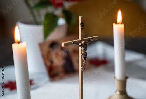 cross with Jesus crucified and two lit candles on a white tablecloth with a Christmas tree in the background photo