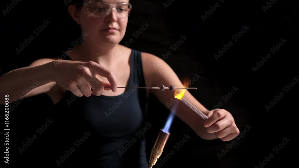 Young woman working with molten glass to make beads over a flame. Young woman working with molten glass to make beads over a flame.