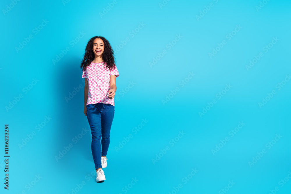 Full length photo of adorable lovely girl wear print t-shirt walking empty space isolated blue color background Full length photo of adorable lovely girl wear print t-shirt walking empty space isolated blue color background