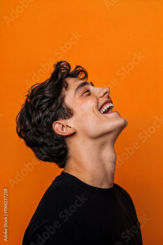 Obraz na płótnie The image shows a person with curly hair and a black shirt, laughing with their head tilted back against an orange background w salonie