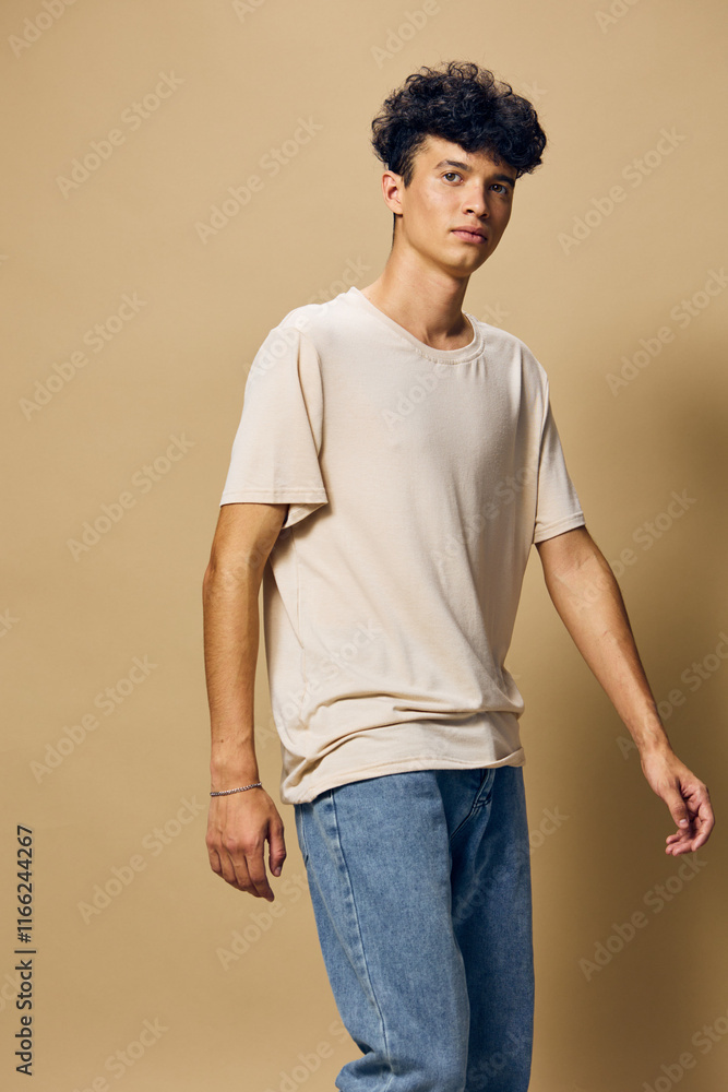 Casual young man in a light beige t shirt and blue jeans against a plain beige background, exuding a relaxed and modern style, perfect for fashion related concepts Casual young man in a light beige t shirt and blue jeans against a plain beige background, exuding a relaxed and modern style, perfect for fashion related concepts