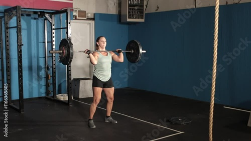 Young female weight lifter lifting barbell from floor over her head.