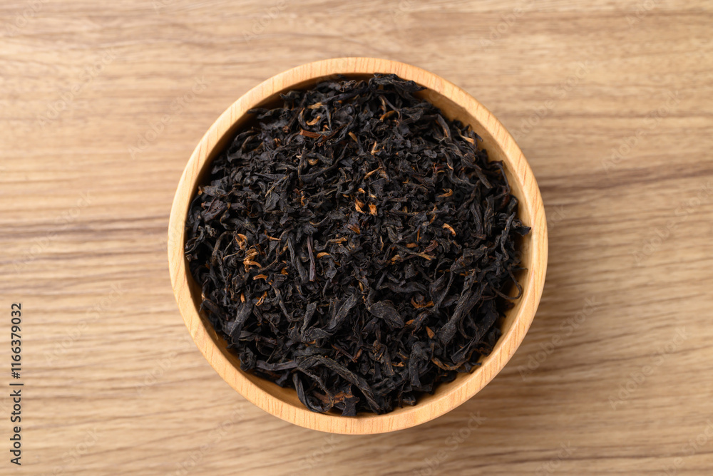 Dried black tea leaves in bowl on wooden background, Table top view