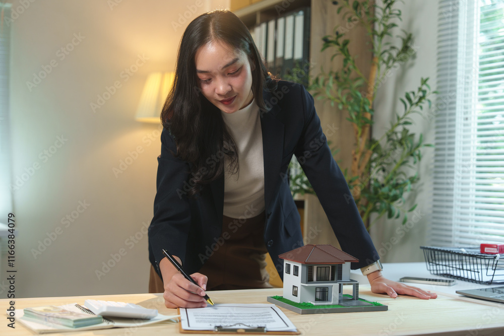 Young businesswoman working as a real estate agent, signing a contract for a new house sale while a scale model of the property sits on her desk, highlighting her professionalism Young businesswoman working as a real estate agent, signing a contract for a new house sale while a scale model of the property sits on her desk, highlighting her professionalism