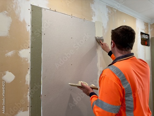 A man uses a putty knife and plaster to smooth a wall seam on freshly installed drywall sheeting used to close up a doorway, preparing the surface for painting during a DIY home renovation project.