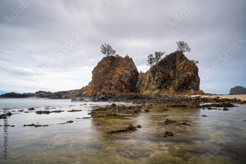 Dramatic coastal scene of Diguisit, Aurora featuring rugged rock formations, under a fast-moving, moody clouds. Calm water reflects the rich tones of the sky, creating a striking and seascape. photo