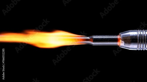 Flame ignites from a metal nozzle creating a bright orange burst in a dark environment during a high-precision operation