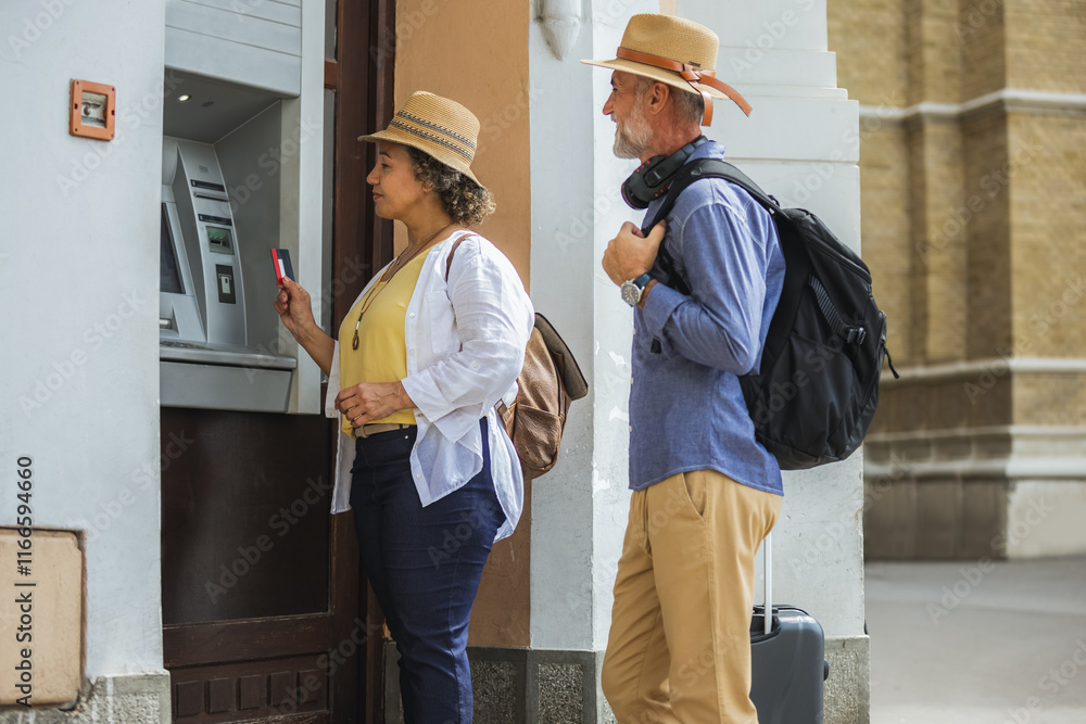 Senior couple of tourists is withdrawing money from an ATM in a bustling city setting. They appear focused and content, preparing for their next adventure during their travels. Senior couple of tourists is withdrawing money from an ATM in a bustling city setting. They appear focused and content, preparing for their next adventure during their travels.