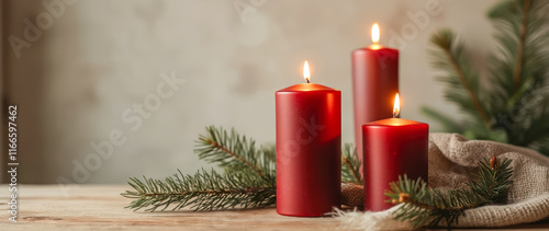 three burning red candles with evergreens
