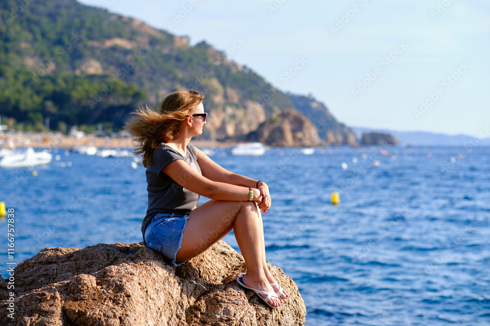 A woman sits on a rock and looks out to sea. A woman sits on a rock and looks out to sea.