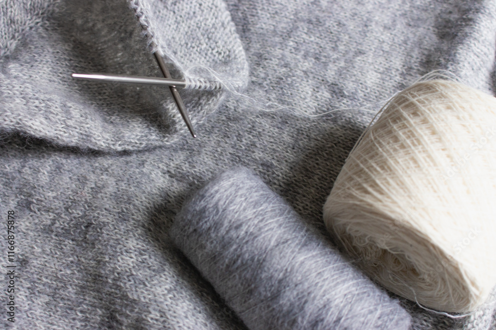 Grey melange knitting sweater with knitting needles. Mix of grey wool and white cashmere with needles. Knitting pattern background. Knitting lifestyle. Cozy hobby. Warm knitwear. Craft product concept