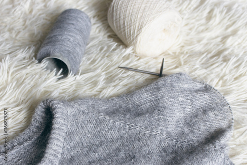 Grey melange knitting sweater with knitting needles. Mix of grey wool and white cashmere with needles. Knitting pattern background. Knitting lifestyle. Cozy hobby. Warm knitwear. Craft product concept