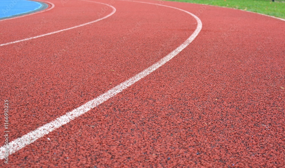 Fototapeta premium red running track curve with white lines and green grass in right side
