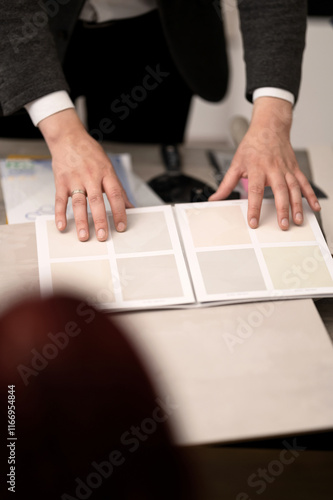 Catalog with paints palette for interior design on table. Designer consults client in design studio. Person chooses samples of paints for walls. Varnishes, plasters, backgrounds, wallpapers, facades.