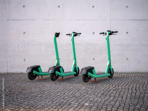 green e-scooters parked on a cobblestone pavement against a minimalist concrete wall photo