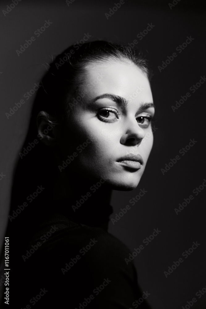 Thoughtful young woman in black turtleneck, illuminated dramatically from the side, creating a striking monochrome portrait. Introspection and beauty concept. Thoughtful young woman in black turtleneck, illuminated dramatically from the side, creating a striking monochrome portrait. Introspection and beauty concept.