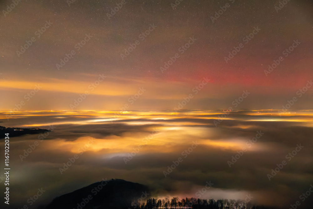 Obraz premium Feuerwerkslichter unter dem Nebelmeer. Silvester Feuerwerk 2024 und roter Aurora Borealis Polarlichter. Auf dem Breitenstein, Schwäbische Alb bei Ochsenwang. Blick Richtung Stuttgart und Hörnle.