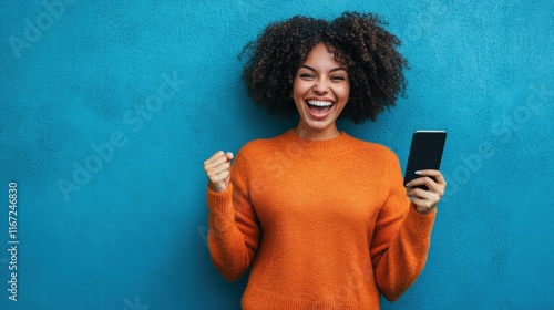 Excited young African woman celebrating success with a phone in hand – joy and triumph on a blue background