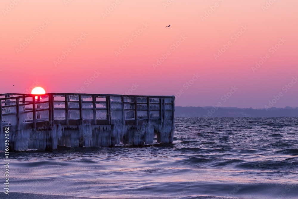Winter seascape with ice covered jetty at the Baltic Sea at sunrise.