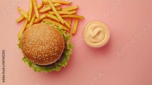 Overhead view of a hamburger with french fries and a side of sauce on a pink background.. photo