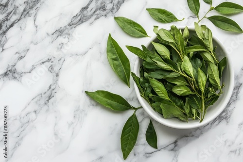 Fresh green curry leaves in a white bowl on a marble surface. photo