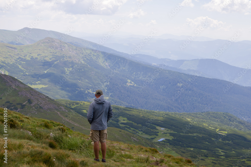 Hiker standing on top of a mountain and looking at the valley Hiker standing on top of a mountain and looking at the valley