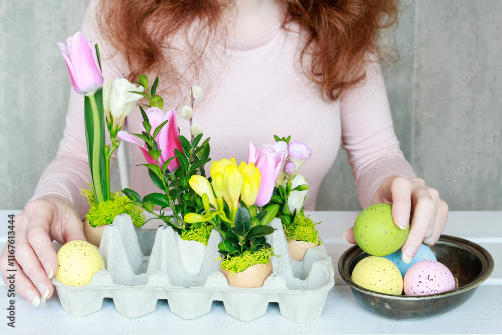 Florist at work: woman shows how to make Easter floral decoration with colorful eggs, tulips, freesias and buxus. Step by step, tutorial.