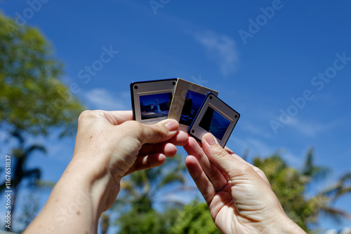 A photo of hands holding slides against the sky.
 photo