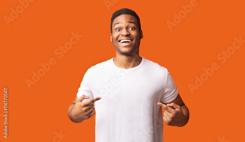 Clothes Template. Happy black man pointing at white t-shirt, mockup for logo or branding design