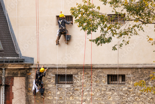 Deux travailleurs cordistes rénovent une façade d'immeuble à Paris