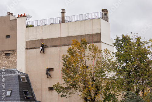 Deux travailleurs cordistes rénovent une façade d'immeuble à Paris