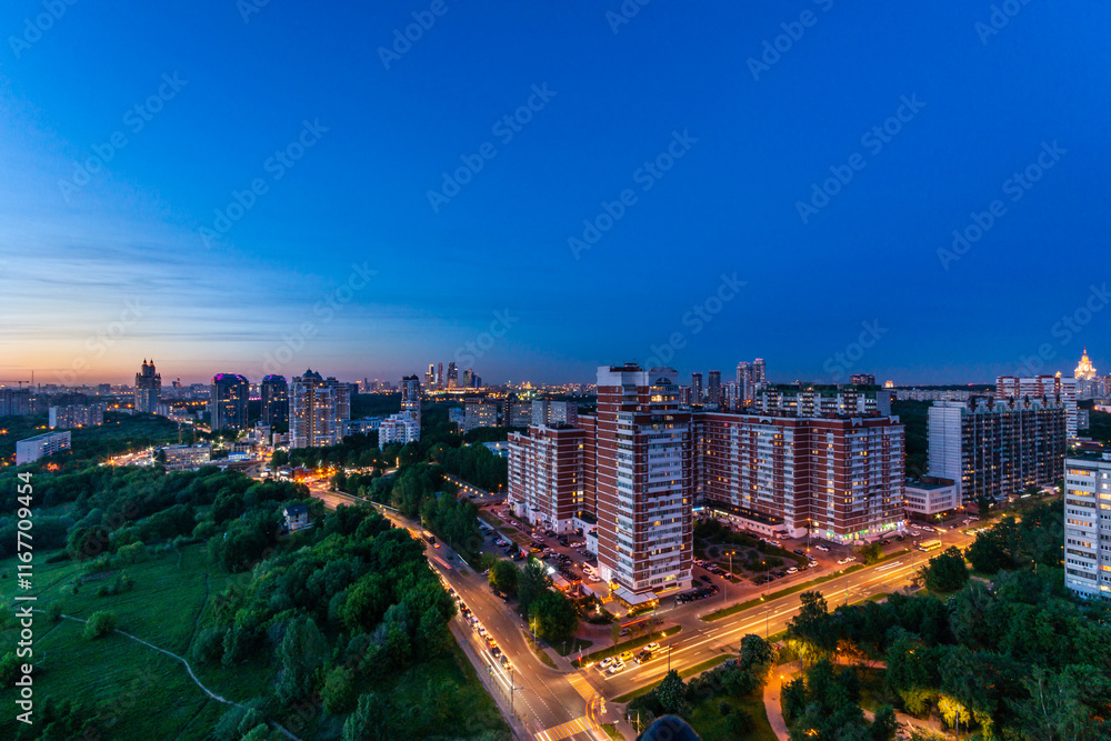 Obraz premium Urban landscape showcases high-rise buildings transitioning into night with city lights twinkling. A large green park contrasts the vibrant skyline, creating a peaceful atmosphere.