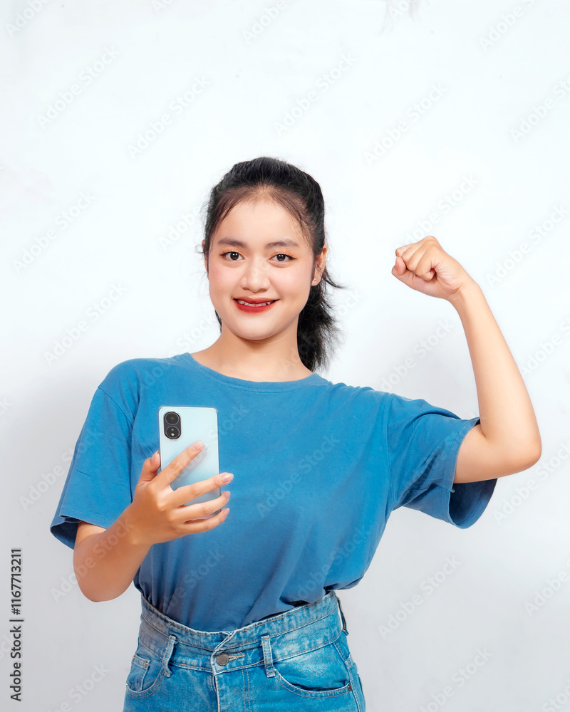 Overjoyed young Asian woman is raising her hands in the air with happy successful expression with holding phone Overjoyed young Asian woman is raising her hands in the air with happy successful expression with holding phone