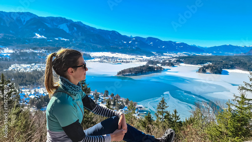 Hiker woman on top of Taborhoehe viewing platform in Carinthia, Austria, Europe. Surrounded by snow capped Karawanks mountains. Frozen Lake Faak. Alpine Landscape in frosty winter in Austrian Alps photo