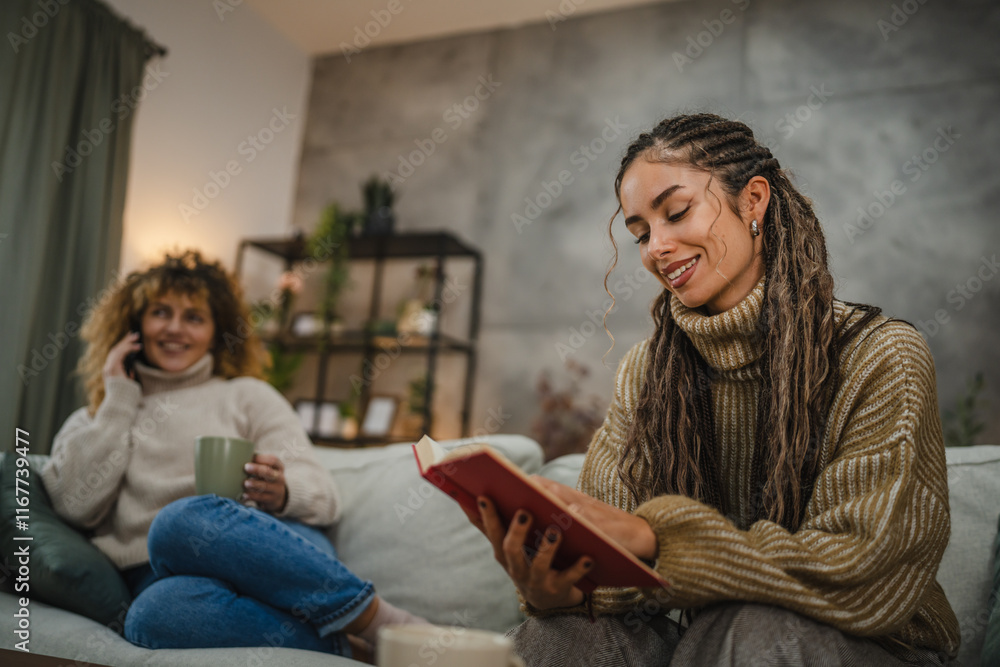 female friends enjoy on sofa one read a book while other use cellphone female friends enjoy on sofa one read a book while other use cellphone