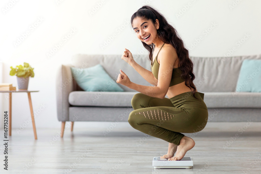 Happy Indian woman sitting on scales, gesturing YES, satisfied with her weight loss result at home, full length. Young Hindu lady celebrating her achievement, successful in slimming Happy Indian woman sitting on scales, gesturing YES, satisfied with her weight loss result at home, full length. Young Hindu lady celebrating her achievement, successful in slimming