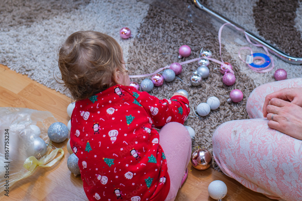 Fototapeta premium The little child playing with Christmas balls, with mother in nearby. Christmas holiday spirit 