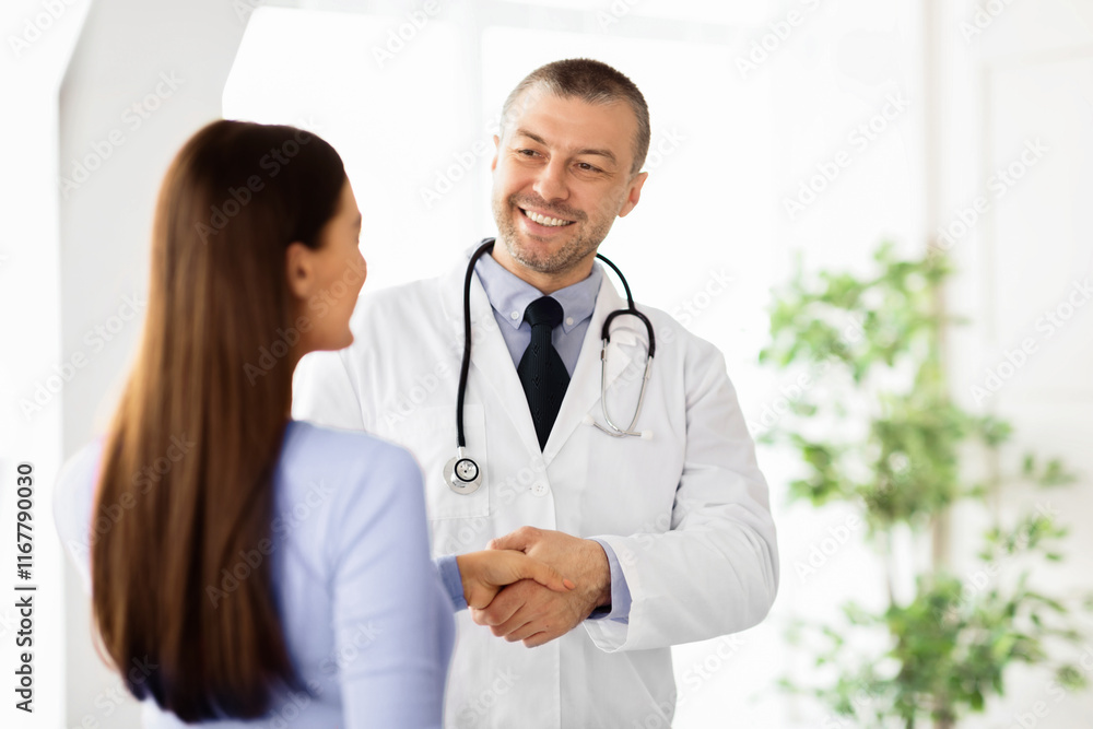 Professional Help. Portrait of smiling middle aged general practitioner shaking hands with woman standing at clinic or hospital. Patient greeting her doctor. Healthcare and Medicine Concept Professional Help. Portrait of smiling middle aged general practitioner shaking hands with woman standing at clinic or hospital. Patient greeting her doctor. Healthcare and Medicine Concept