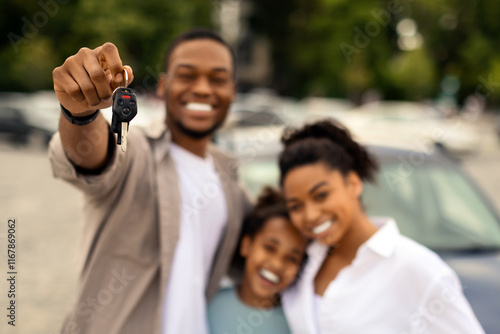 Car Purchase. Cheerful African American Family Holding Auto Key To Camera Standing Outside Near New Vehicle. Automobile Owners Concept. Selective Focus On Keys