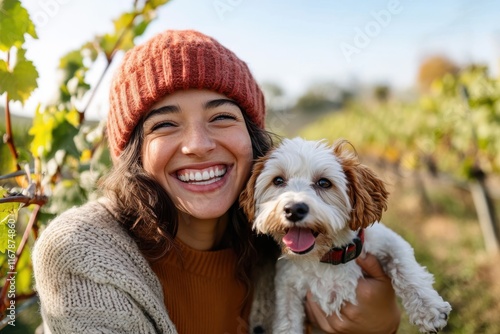 Joyful girl in a cozy beanie shares a sunny moment with her fluffy dog among vineyard rows on a bright autumn day photo