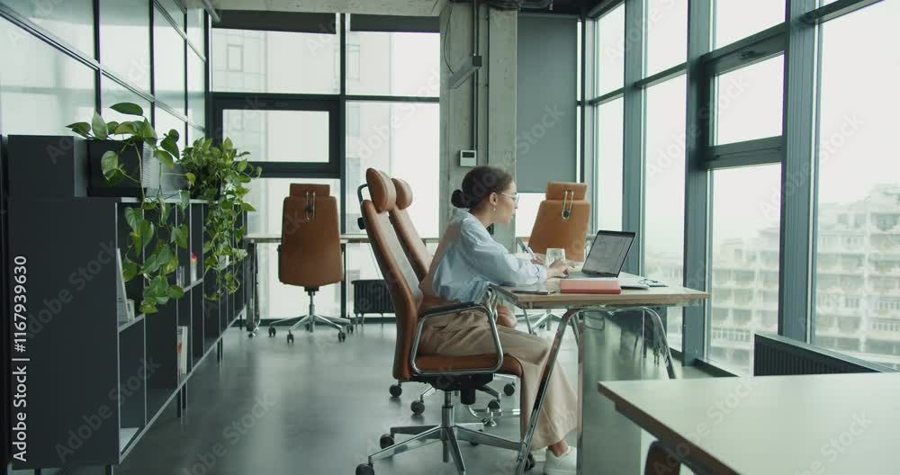modern office space with a young woman in professional attire working on a laptop, surrounded by large windows, natural light, and contemporary furniture modern office space with a young woman in professional attire working on a laptop, surrounded by large windows, natural light, and contemporary furniture