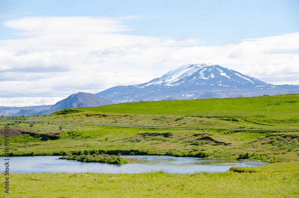 A snow covered mountain rises over the vibrant green valley in Iceland A snow covered mountain rises over the vibrant green valley in Iceland