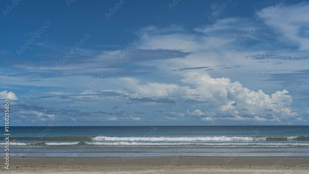 Fototapeta premium Beautiful seascape. The waves of the turquoise ocean roll towards the shore, foaming on the sandy beach. Picturesque clouds in the blue sky. Malaysia. Borneo. Kota Kinabalu.