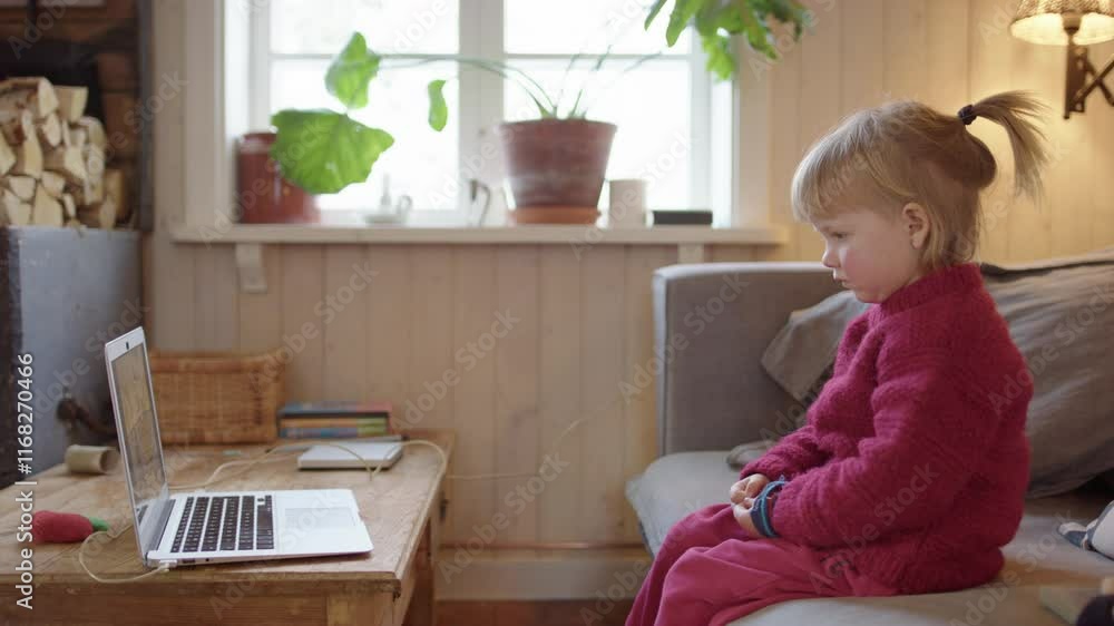Cute preschooler girl on living room sofa watching cartoons on laptop, profile Cute preschooler girl on living room sofa watching cartoons on laptop, profile