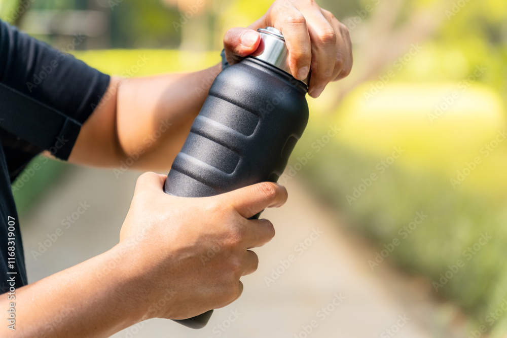 Naklejka premium A person wearing a black shirt opening a black water vacuum flask in a park setting