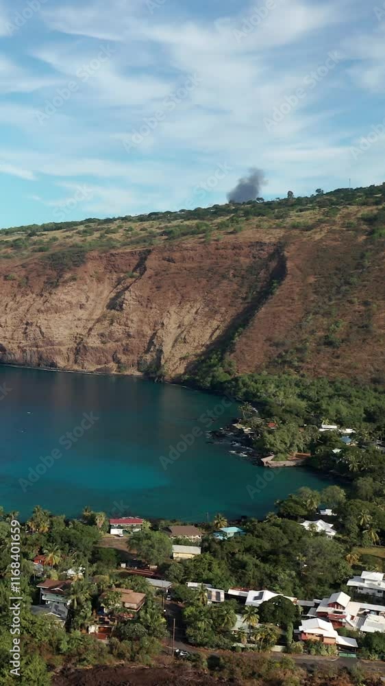 A calm vertical shot of Captain Cook, Hawaii, showing cliffs, water, and smoke rising A calm vertical shot of Captain Cook, Hawaii, showing cliffs, water, and smoke rising