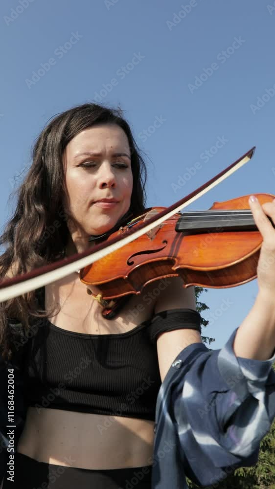 A young girl plays the violin amidst stunning mountain scenery. Surrounded by towering trees, she enjoys the warmth of summer while sharing her musical talent in a serene natural setting. vertical vid A young girl plays the violin amidst stunning mountain scenery. Surrounded by towering trees, she enjoys the warmth of summer while sharing her musical talent in a serene natural setting. vertical vid