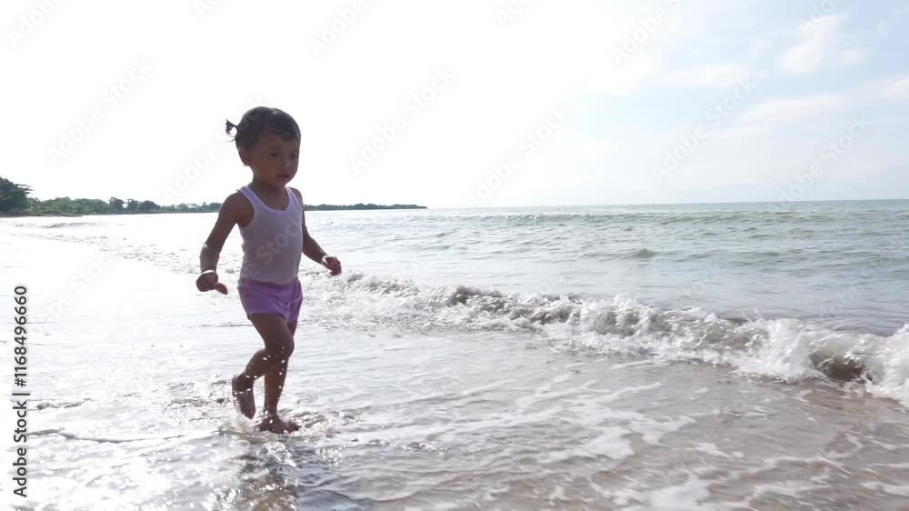In slow motion, an Asian little girl running joyfully along the sandy beach on a summer day. Adorable girl 3 years old enjoy playing on beach runs. In slow motion, an Asian little girl running joyfully along the sandy beach on a summer day. Adorable girl 3 years old enjoy playing on beach runs.
